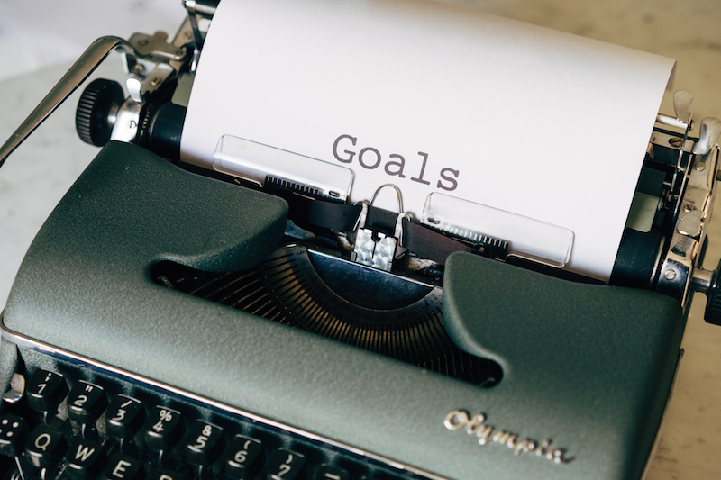 An old fashioned typewriter with a piece of paper loaded into it, with the word "Goals" typed onto the paper.