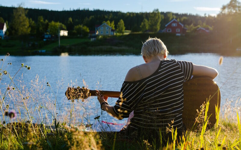 Woman playing guitar outdoors, by a lake.